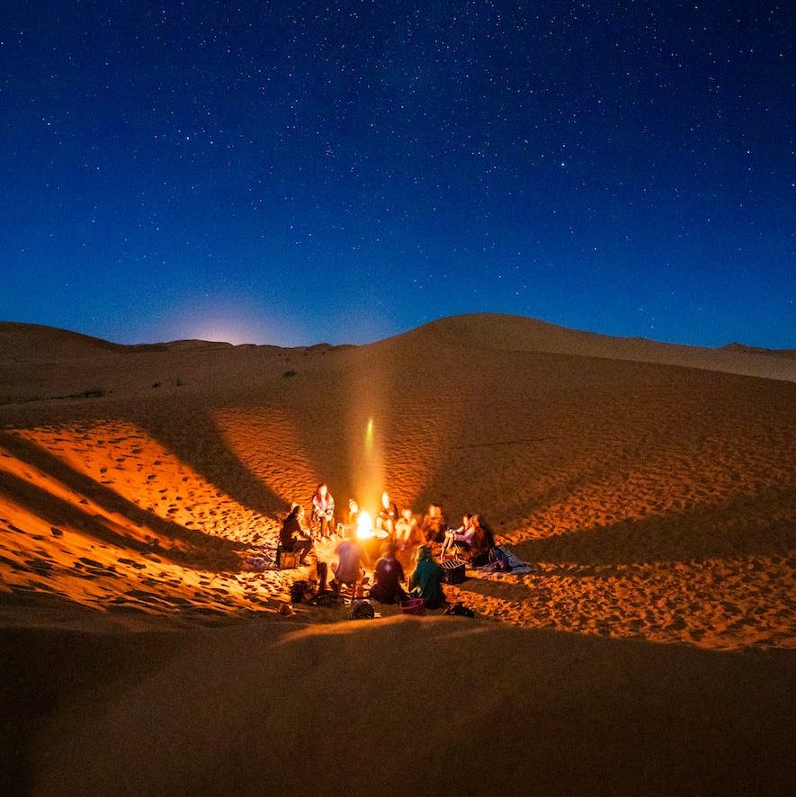 les gens assis devant un feu de joie dans le desert pendant la nuit
